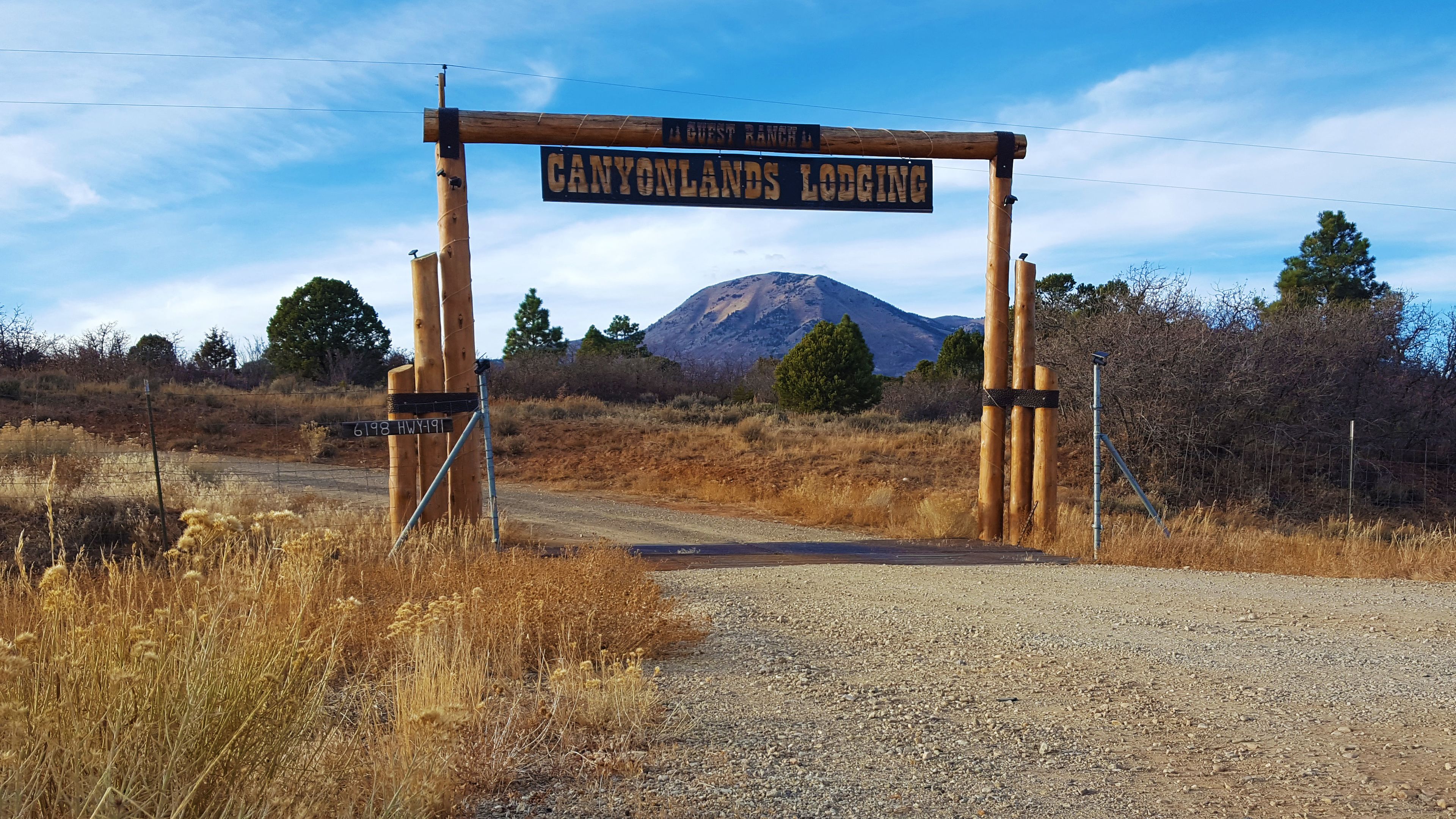 A wooden sign with "CANYONLANDS LODGING" and "A GUEST RANCH" written on it, with a mountain in the background.