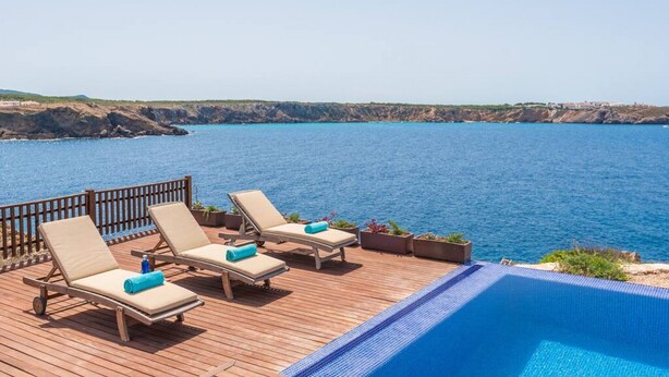 Um deck de madeira com espreguiçadeiras e piscina com vista para a costa.