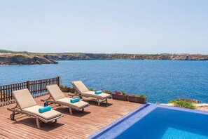 A wooden deck with lounge chairs and a pool overlooking a coastal area. - Villa Marta · Villa Marta❤frontline with great seaview, pool, AC (Es Mercadal)