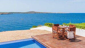 Um deck de madeira com piscina e área de estar ao ar livre, com vista para o mar azul e límpido.