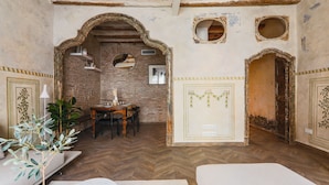 Ein Zimmer mit Fischgrätparkett, einer Ziegelwand, einem Holztisch mit Stühlen und einem großen, bogenförmigen Durchgang.