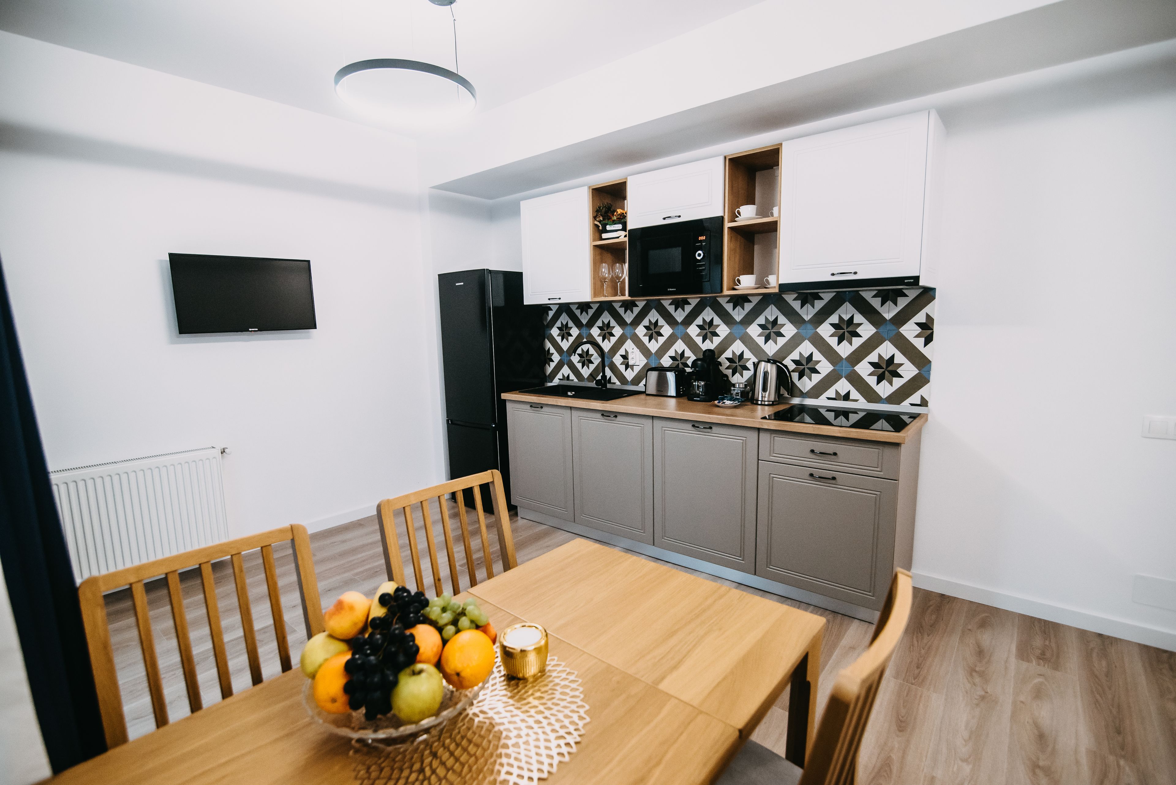 Een moderne keuken met een eettafel gedekt voor twee personen, een schaal met fruit en een flatscreen televisie aan de muur.