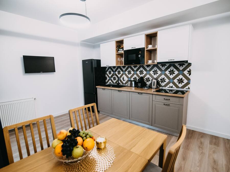 Een moderne keuken met een eettafel gedekt voor twee personen, een schaal met fruit en een flatscreen televisie aan de muur.