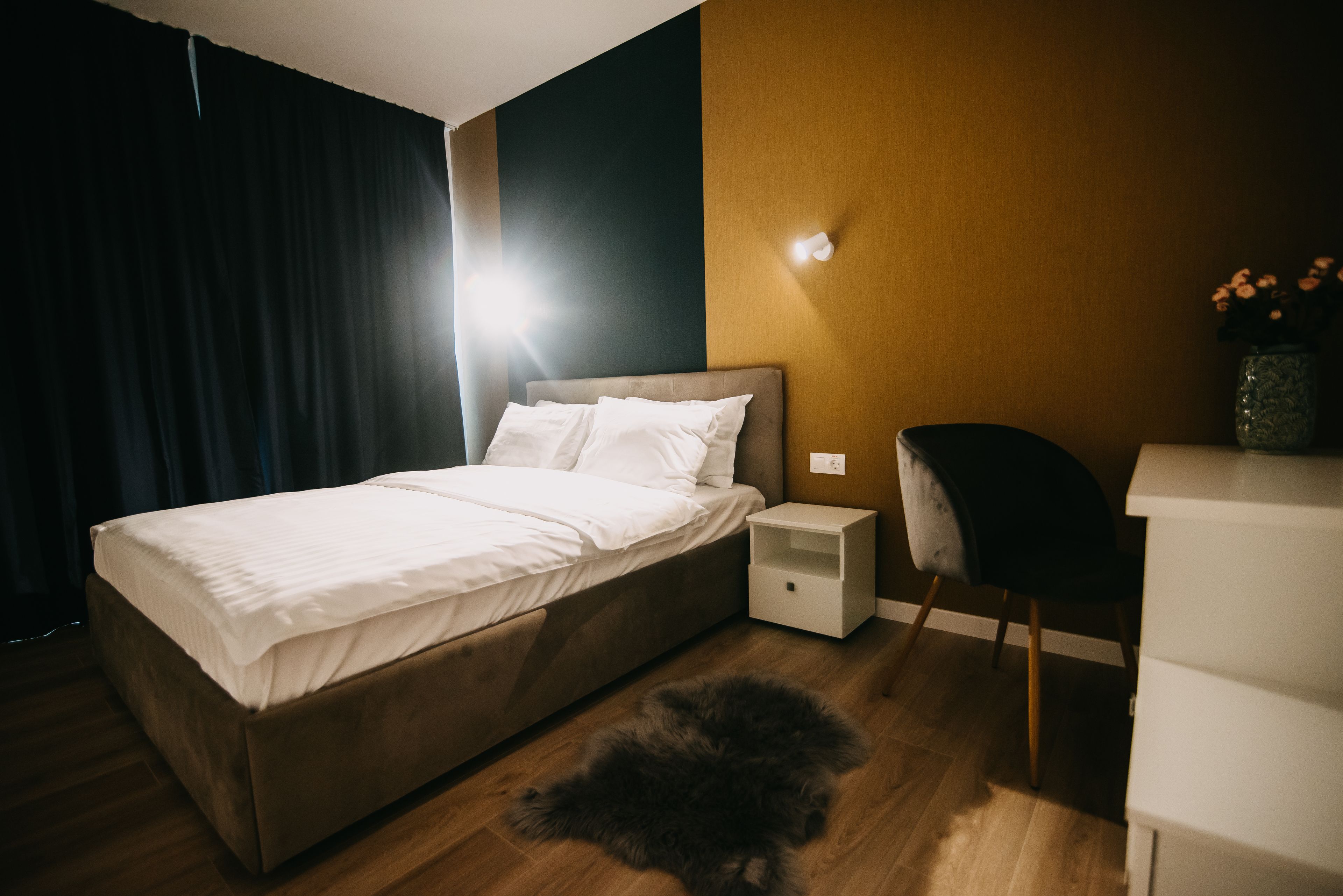 A modern bedroom with a bed, bedside table, chair, and a small rug.