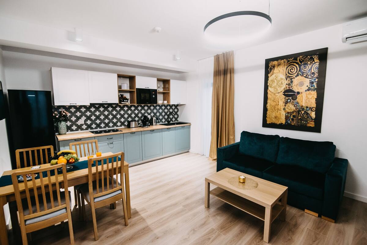 A modern living room with a dining area, a kitchen in the background, and a large abstract painting on the wall.