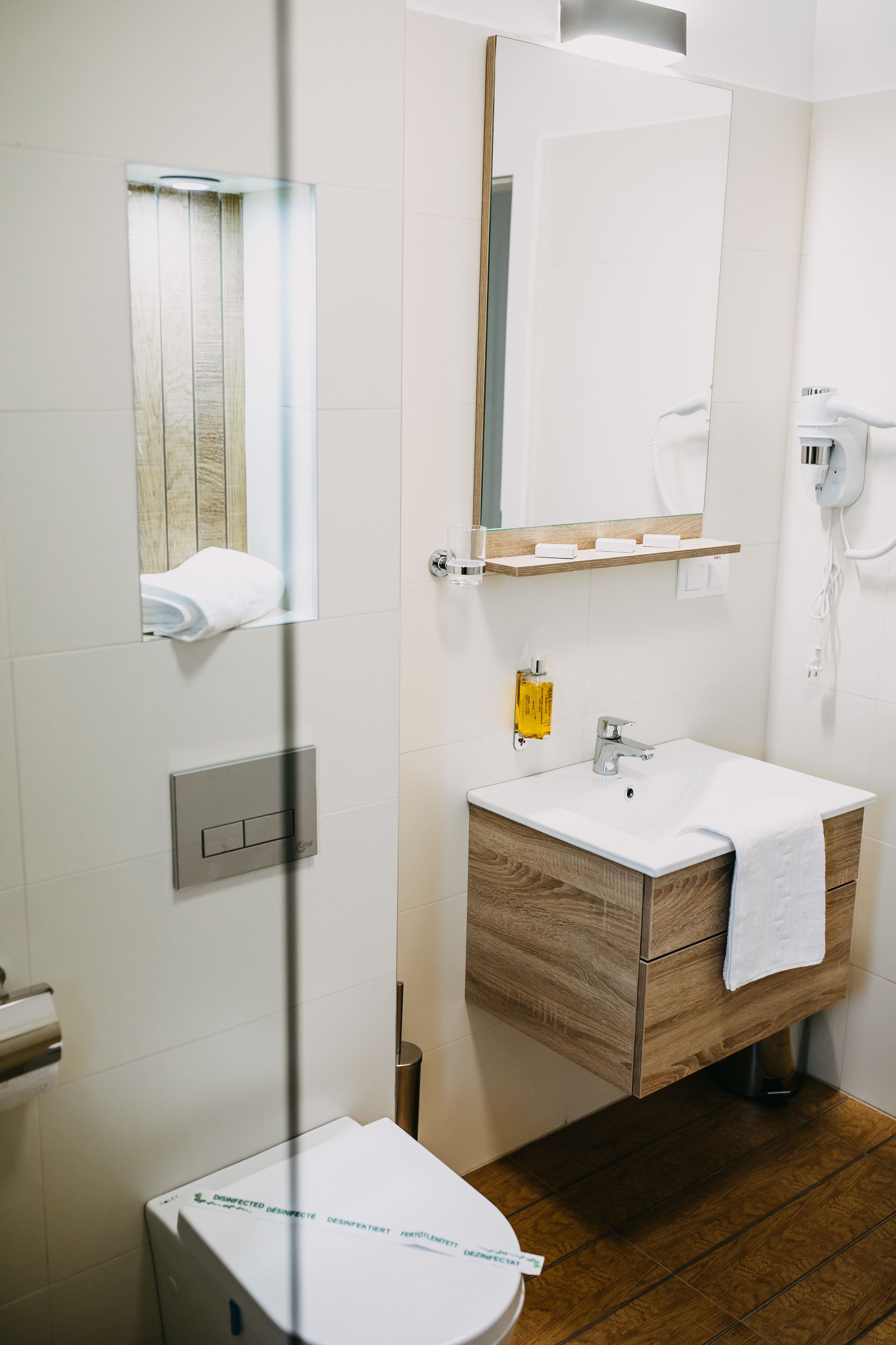 A modern bathroom with a wooden vanity, a white sink, a mirror, and a towel hanging on the wall.