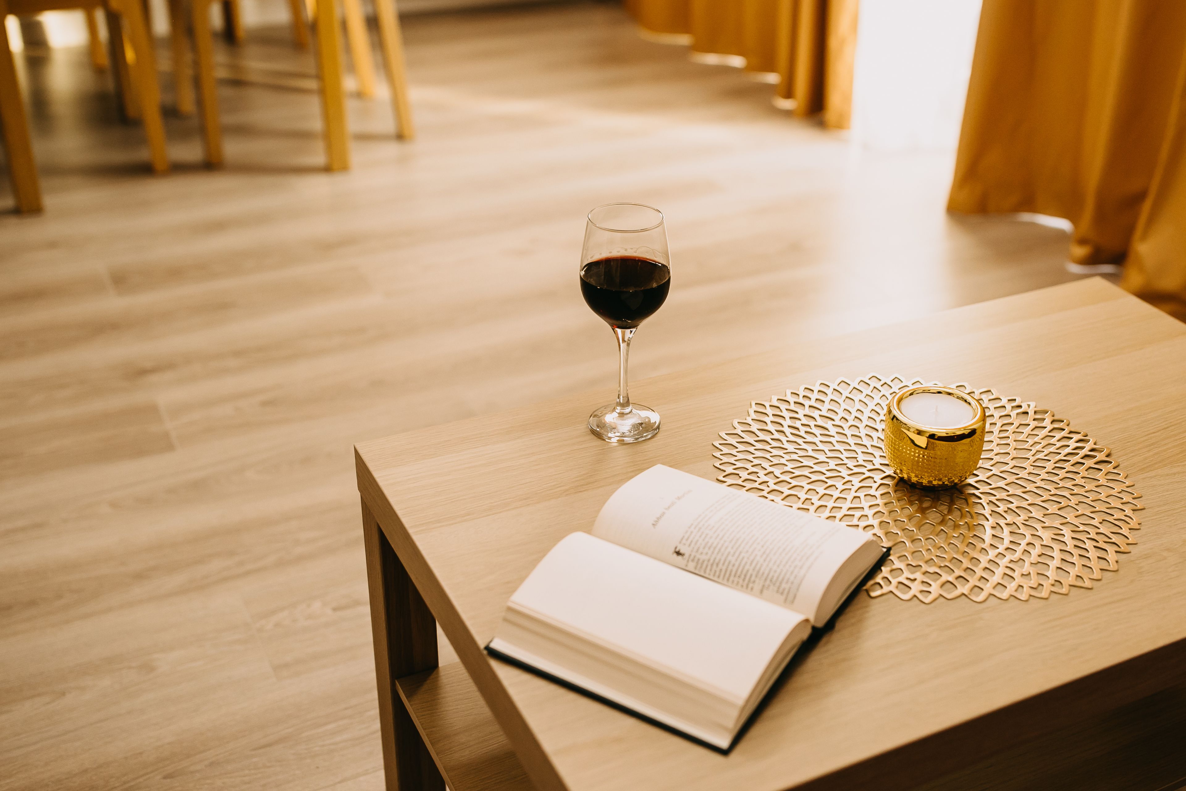 A wooden table with a book, a glass of red wine, and a decorative candle holder.