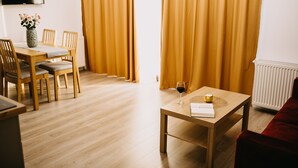A modern living room with a wooden dining table, four chairs, a small coffee table with a book and a glass of wine, and a red sofa. - Gaudi Accommodation (Cluj-Napoca)