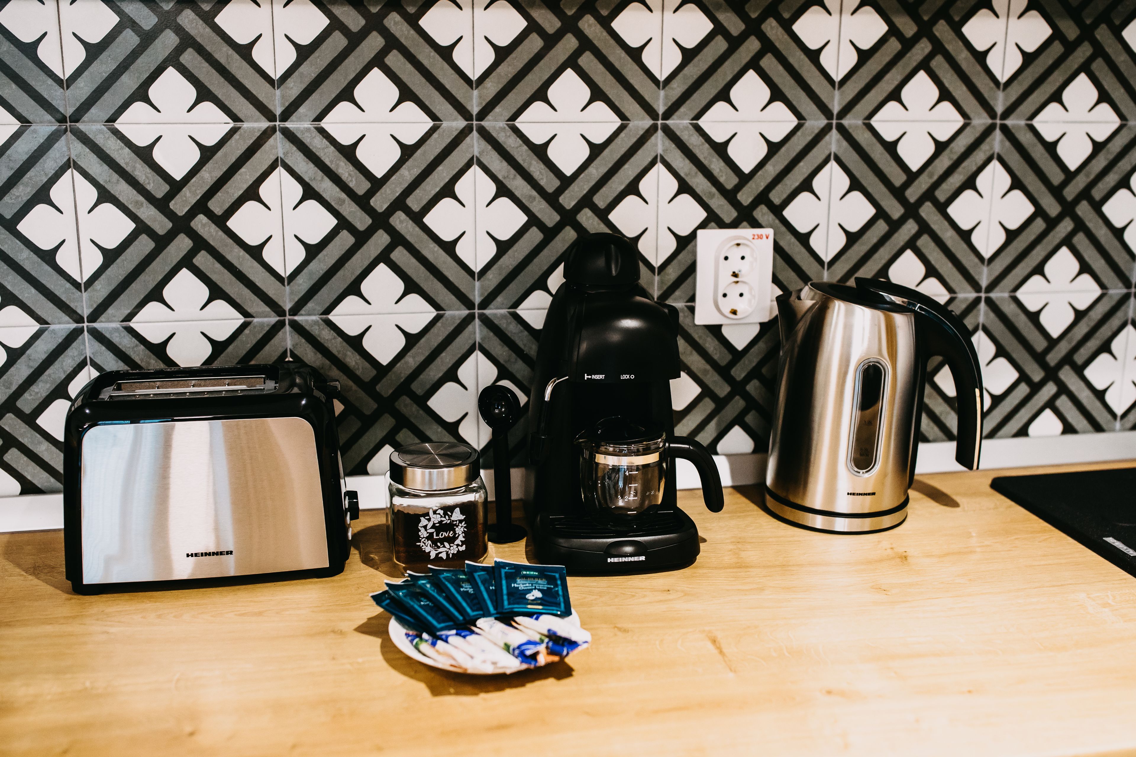 A kitchen counter with a toaster, a coffee maker, a kettle, and a plate with coffee pods.