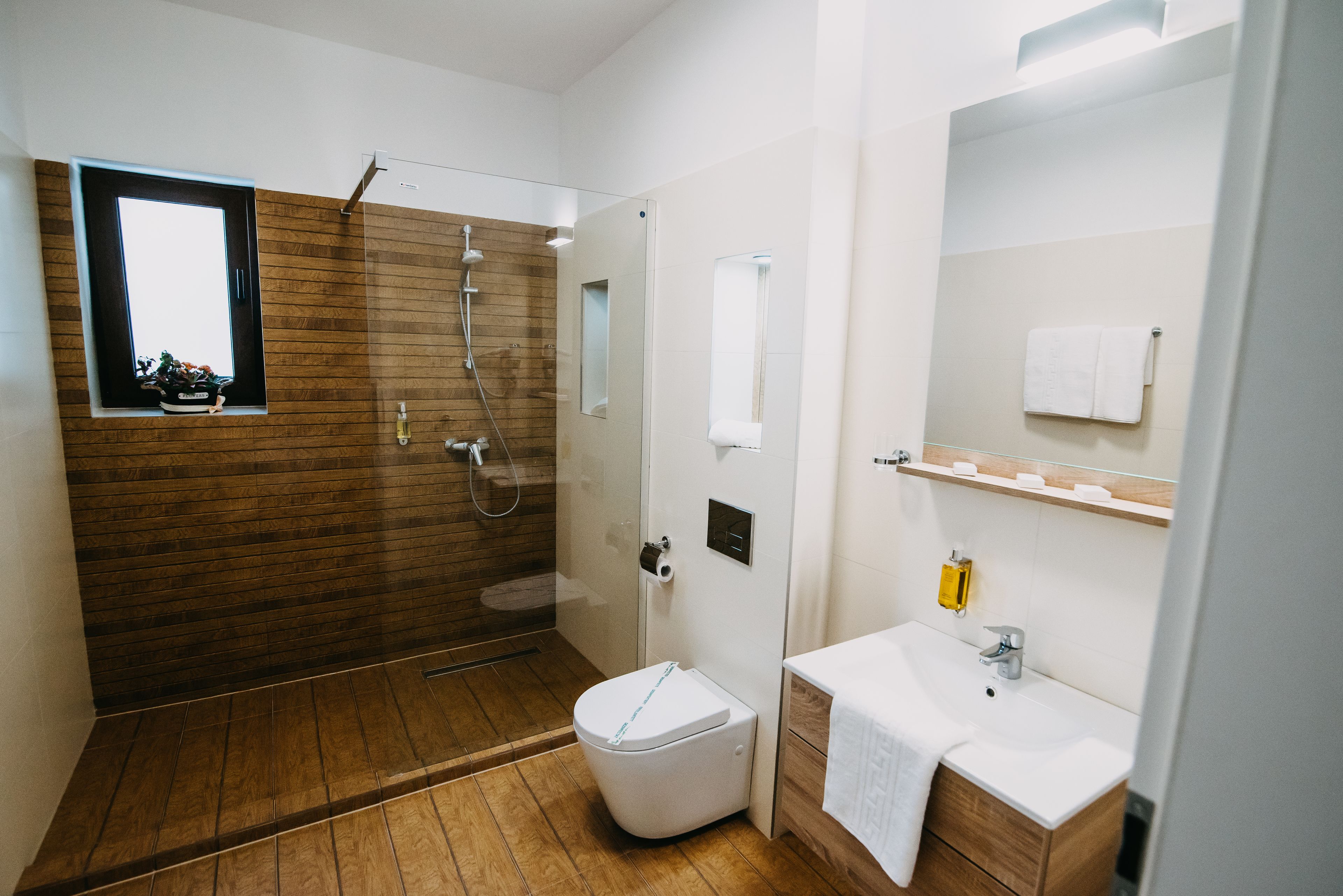 Un bagno moderno con pavimento in legno, cabina doccia in vetro, water bianco, lavandino con specchio e porta asciugamani.