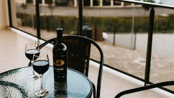 A round glass table with a bottle and two wine glasses on a balcony overlooking a residential area.