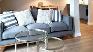 Ein modernes Wohnzimmer mit einem grauen Ecksofa, einem Glastisch und einer Pendelleuchte.