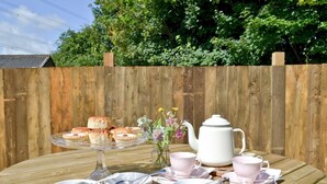Une table en bois, mise avec des tasses à thé, des soucoupes, une théière, ainsi qu’un plateau de scones et de pâtisseries.