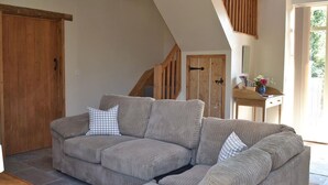 Un salon avec un canapé d’angle, une porte en bois et un escalier.