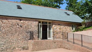 Un bâtiment en pierre doté d’un toit en pente et d’un petit porche agrémenté d’une rambarde en métal.
