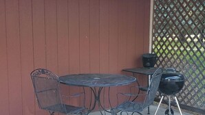 Een terras buiten met een metalen tafel en stoelen, een barbecue en een houten schutting.