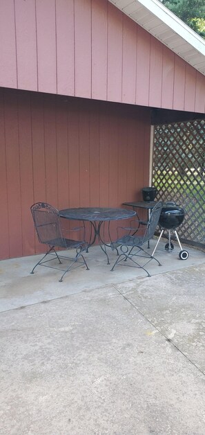 An outdoor patio with a metal table and chairs, a barbecue grill, and a wooden fence.