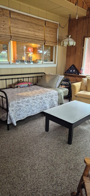 A bedroom with a bed, a nightstand, a dresser, a window with blinds, and a hanging lamp.