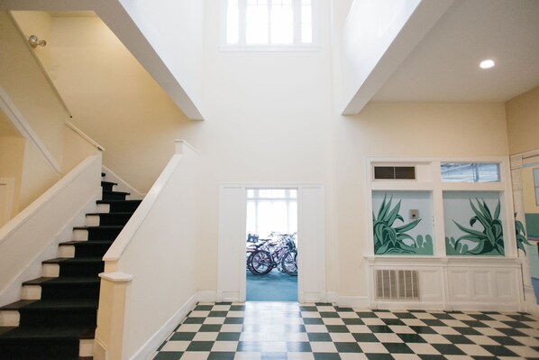 Un hall d’entrée spacieux, doté d’un sol à carreaux, d’un escalier et d’une porte donnant sur une pièce où se trouve un vélo.