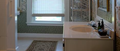 Un baño con un lavamanos blanco, un espejo, una ventana con persianas y una alfombra estampada.