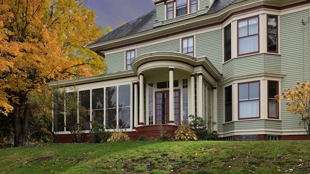 A large, two-story house with a wrap-around porch and a large bay window.