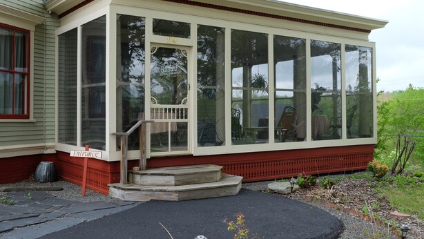 A covered porch with a glass enclosure, a wooden staircase, and a sign indicating an entrance. - Guilford Bed and Breakfast (Guilford)
