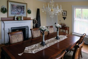 Une salle à manger avec une grande table en bois, des chaises, un lustre et une cheminée.