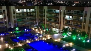 A rooftop pool area with multiple pools, palm trees, and surrounding buildings. - Flat na Praia do Futuro (Fortaleza)