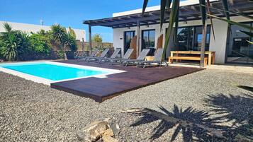 Un área de piscina moderna al aire libre con sillas de descanso y una terraza de madera.