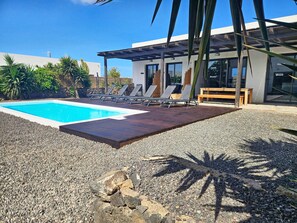 A modern outdoor pool area with lounge chairs and a wooden deck. - MAAR House (La Oliva)