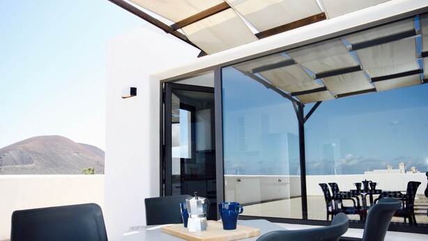 A modern outdoor dining area with a table and chairs, a coffee maker, and a view of the cityscape and mountains. - MAAR House (La Oliva)