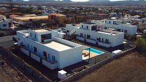 A modern residential area with white buildings, a swimming pool, and a clear view of distant mountains. - MAAR House (La Oliva)