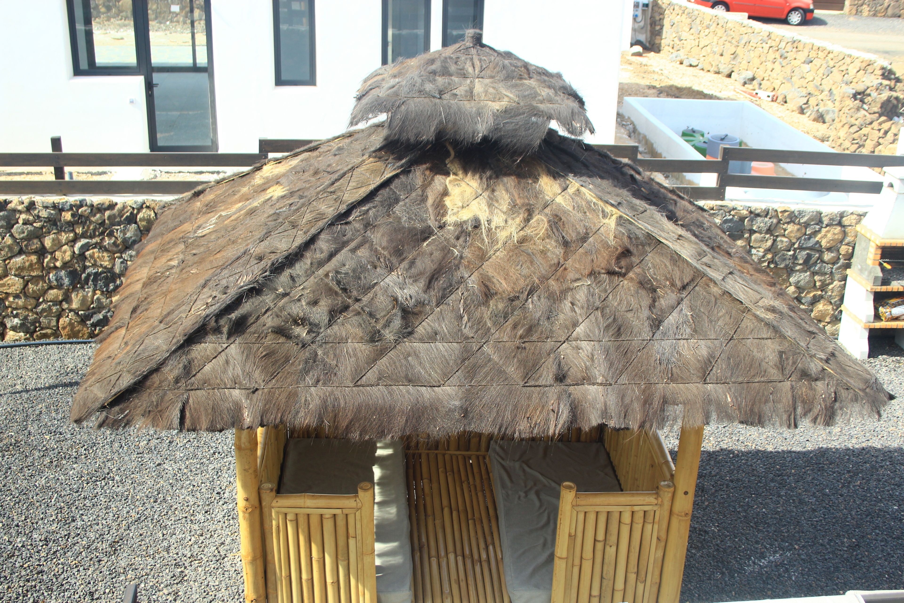 Ein Gebäude mit einem Reetdach, das an einer Steinmauer und einem Gebäude mit Fenstern steht, mit Holzbanken davor.