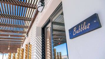 Entrada de un edificio con un letrero que dice 'Bubbles' y una estructura de techo con listones de madera.