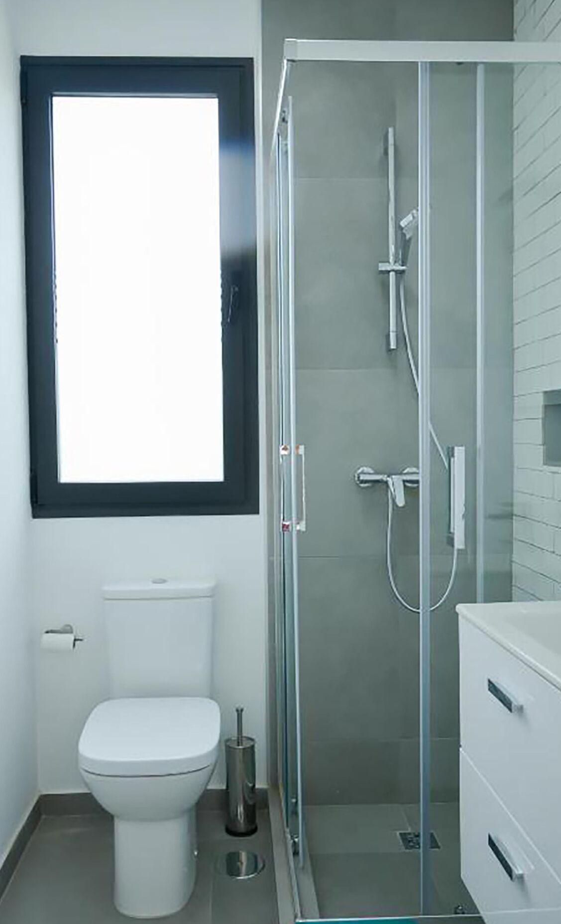 A bathroom with a toilet, a glass-enclosed shower, and a window above the toilet.