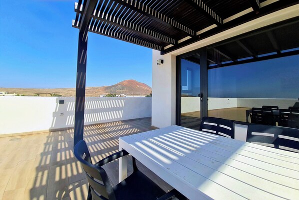 A rooftop terrace with a table and chairs, a pergola, and a view of a mountain. - MAAR House (La Oliva)