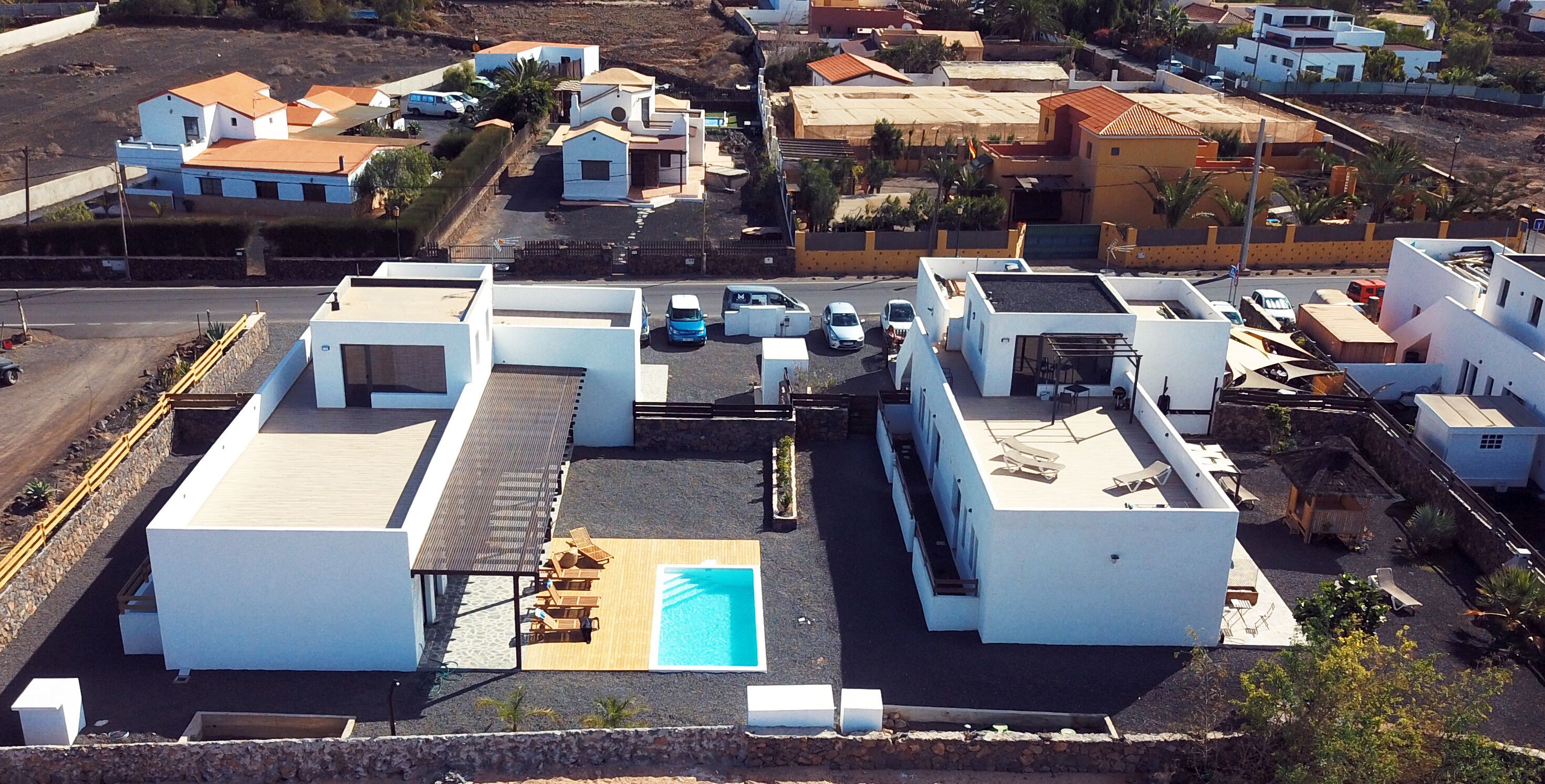 Vista aérea de una zona residencial con casas modernas, una piscina y una calle con automóviles estacionados.