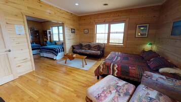 Une cabane en bois avec un grand lit, un canapé et un bureau. Elle comporte deux fenêtres et une porte qui donne sur une autre pièce.