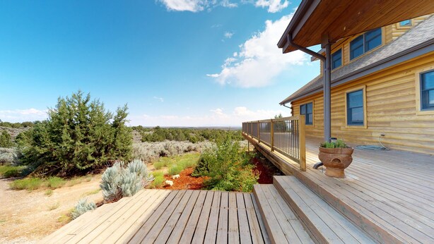 A wooden deck with a view of a natural landscape and a building with large windows. - Mustang Mesa Amazing Views (Blanding)