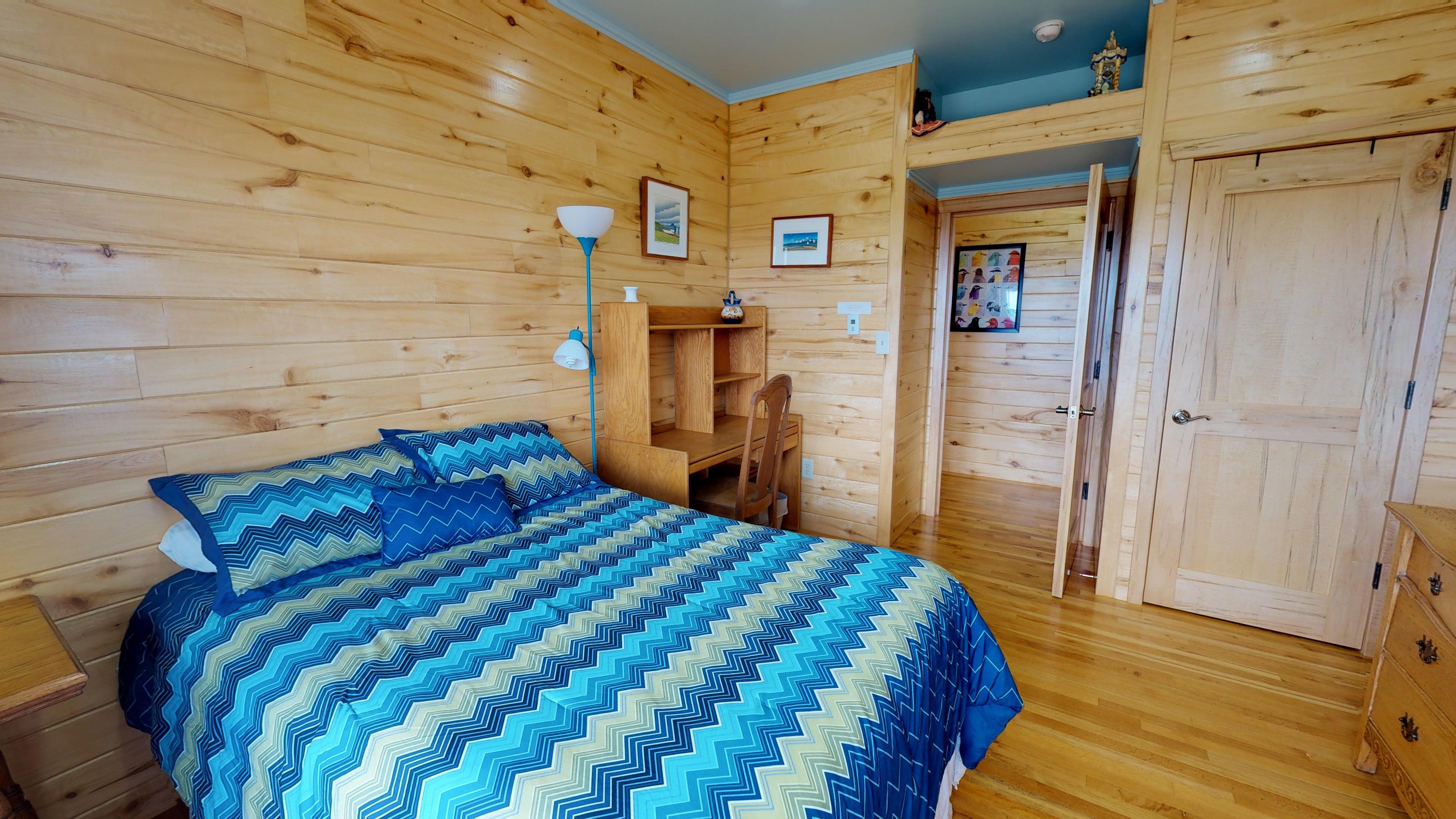 A wooden cabin bedroom with a bed, a desk, and a wardrobe.