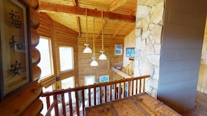 A wooden interior with a stone wall, wooden ceiling beams, and a staircase with a wooden railing. - Juniper Ridge Family Cabin (Blanding)