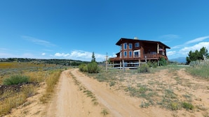 A two-story wooden house with a balcony, surrounded by a dirt road and sparse vegetation. - Juniper Ridge Family Cabin (Blanding)