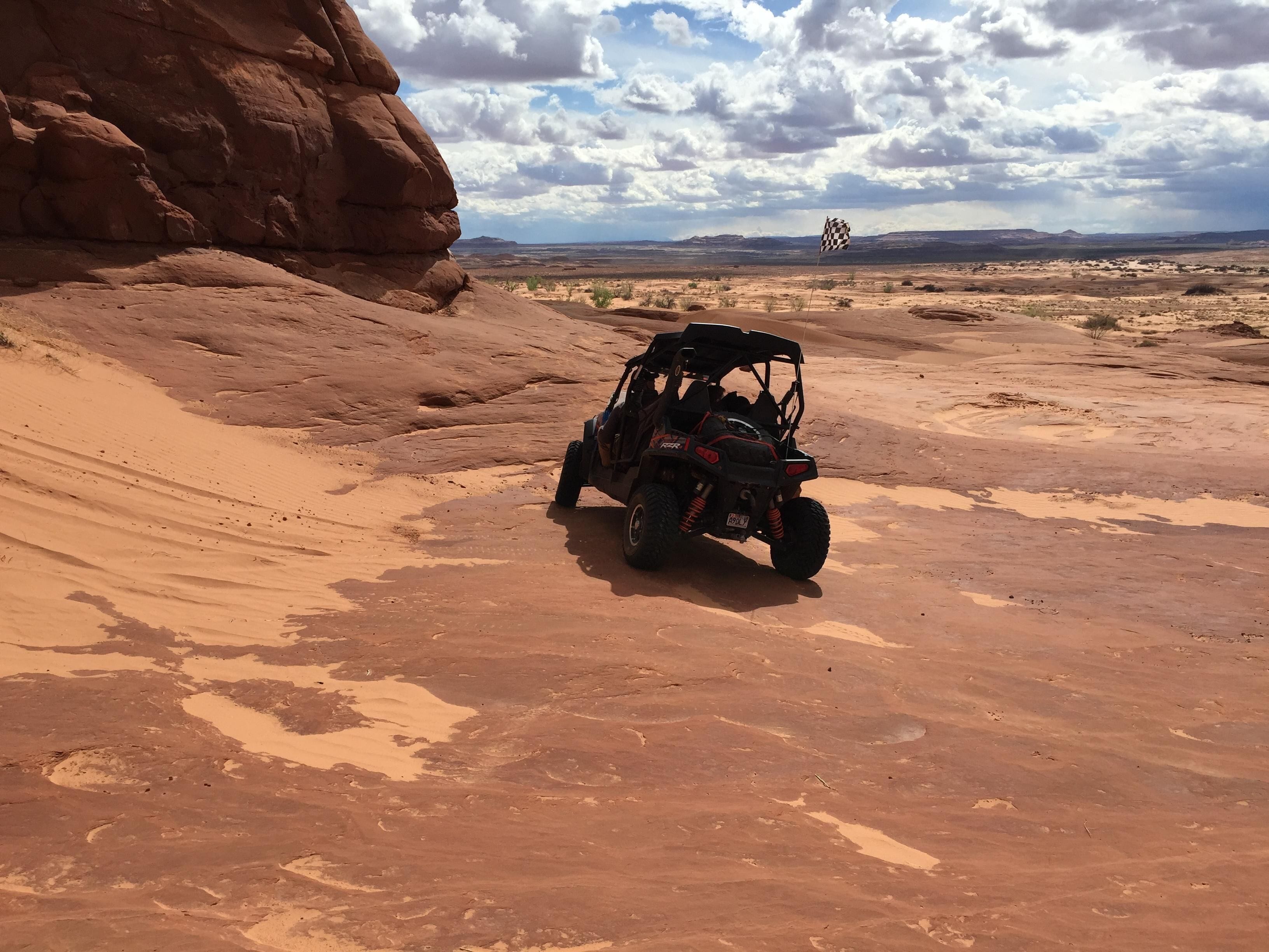 A desert landscape with a red rock formation and a checkered flag in the distance.