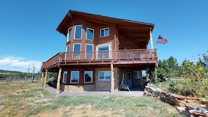 A two-story log cabin with a balcony and an American flag. - Juniper Ridge Family Cabin (Blanding)