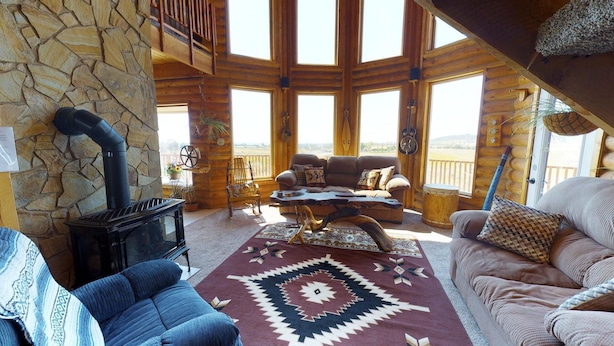 A cozy cabin interior with a stone wall, a fireplace, a sofa, and a view of the outdoors. - Juniper Ridge Family Cabin (Blanding)