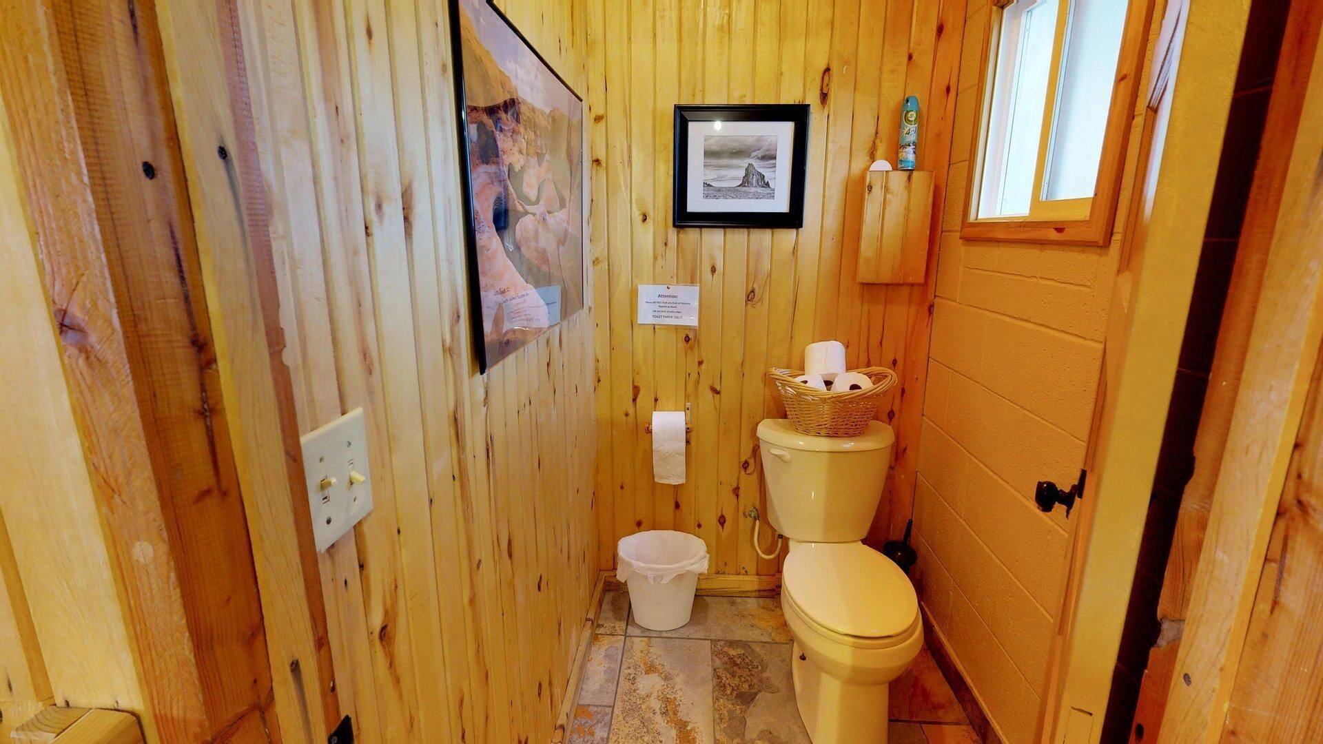 A wooden bathroom with a toilet, a small trash bin, and a framed picture on the wall.