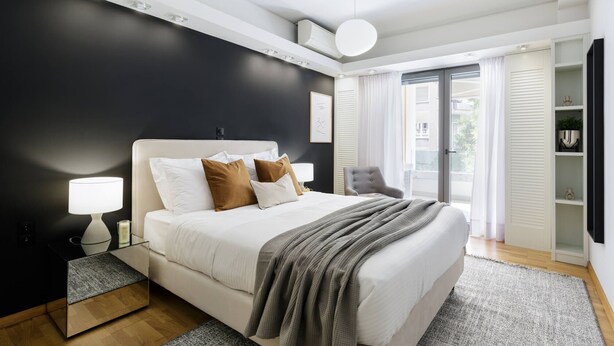 Un dormitorio moderno con una cama grande, lámparas de noche, una silla y vistas al exterior a través de una puerta de cristal.