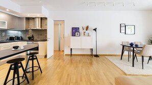 Una cocina moderna con una isla central, taburetes de bar, una zona de comedor con mesa y sillas, y una decoración minimalista.