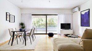 Una sala de estar moderna con sofá, mesa de comedor con sillas, televisor y un ventanal con cortinas.