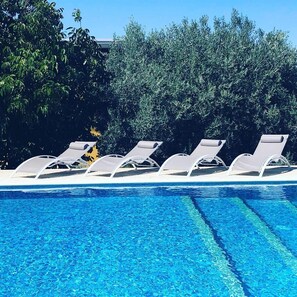 A swimming pool with clear blue water, surrounded by white lounge chairs and dense green foliage. - HEAVEN SUDDENLY HOLIDAY HOUSE (Solarino)